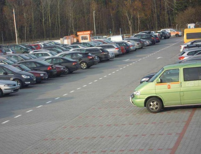 Orange Parking Modlin - Na obrázku je plné parkovisko. Autá stoja na viacerých miestach. Vidno dozornú búdku pri vstupe.