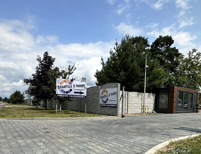 Comienza con nosotros - Aparcamiento en pavimento de adoquines, cercado. Puerta y árboles visibles.