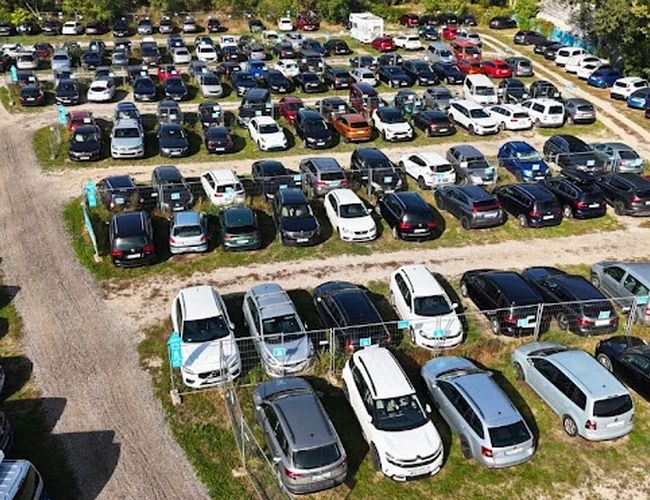 Parktiger Airport Parking 1 - na zdjęciu widać duży, otwarty parking z wieloma zaparkowanymi samochodami. Utwardzone alejki oddzielają rzędy pojazdów. Teren jest niewielkim ogrodzeniem.