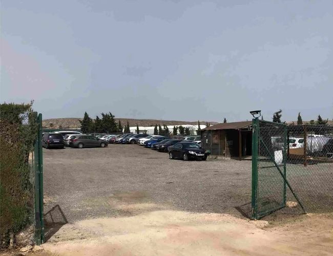 Sunline Parking Covered Valet – Parking ogrodzony siatką. Widać kilka zaparkowanych samochodów. W tle stoi niewielki budynek.