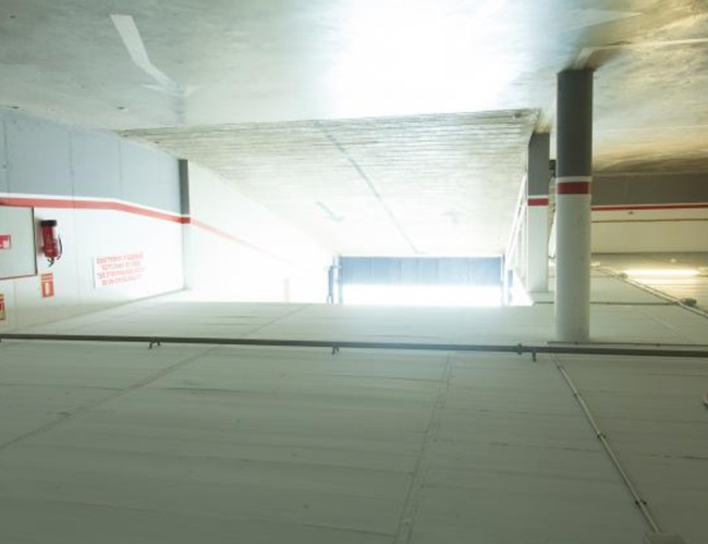 WeParking Valet - Interiér podzemného parkoviska s osvetlením. Viditeľné potrubia a hasičák. Steny sú sivé s červenými akcentmi.