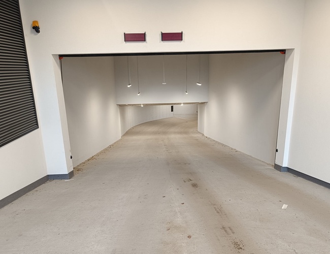 Atrium Garage – vjazd do zastrešeného parkoviska. Steny sú svetlé a hladké. Na strope visia lampy.