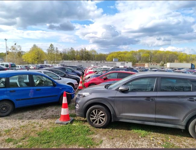 Parking Avanti – Hay numerosos coches en el aparcamiento. Se pueden ver filas de autos y conos. Al fondo, árboles y nubes.