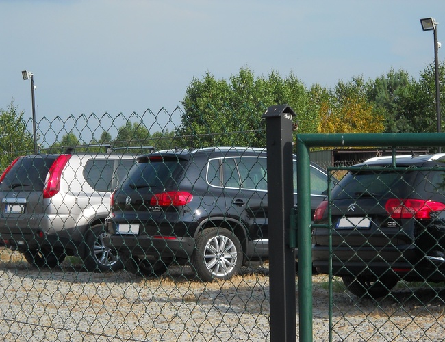 Parkovanie Auto Park - Oplotené námestie s zaparkovanými autami. V pozadí sú viditeľné stromy.