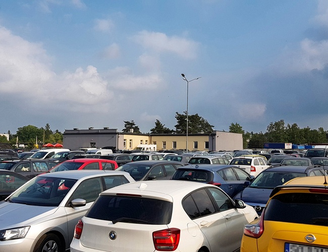 KTW Parking – wiele samochodów stoi na otwartym terenie. W tle są drzewa i budynki. Pogoda jest pochmurna.