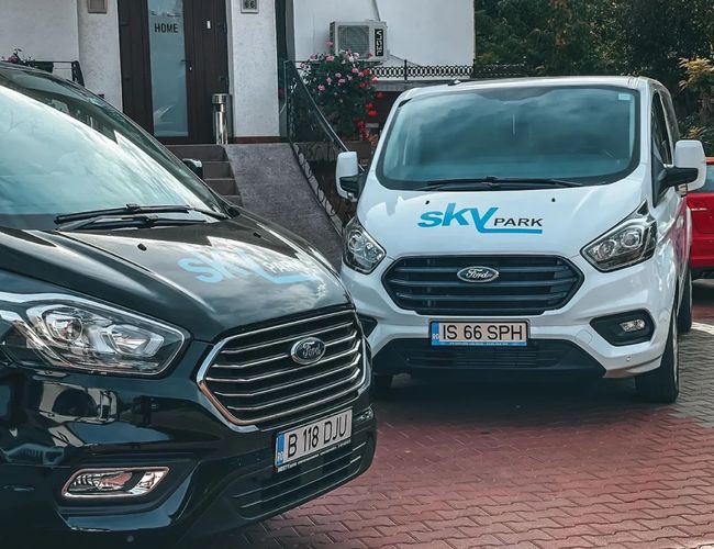 Samochody osobowe oraz biały bus Sky Park stojące na terenie parkingu przy lotnisku w Iași – widok na pojazdy wykorzystywane przez parking.