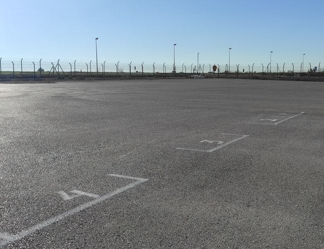 Parking Odkryj-Auto – Asfaltowy plac z oznaczonymi miejscami. Otoczony ogrodzeniem. Oświetlenie latarniami wzdłuż krawędzi.