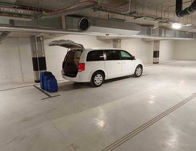 Atriová garáž - Van stojí so založeným zadným vekom. Vedľa ležia dve modré kufre. Na pozadí sú viditeľné ventilačné potrubia.