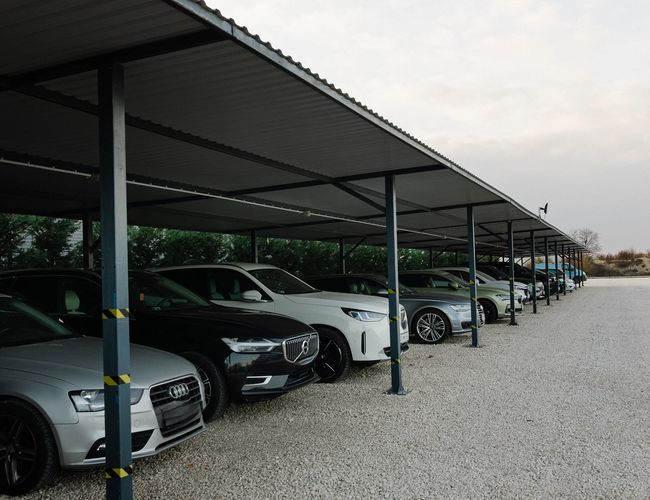 Zadaszony parking długoterminowy z rzędami samochodów osobowych zaparkowanych pod metalową wiatą