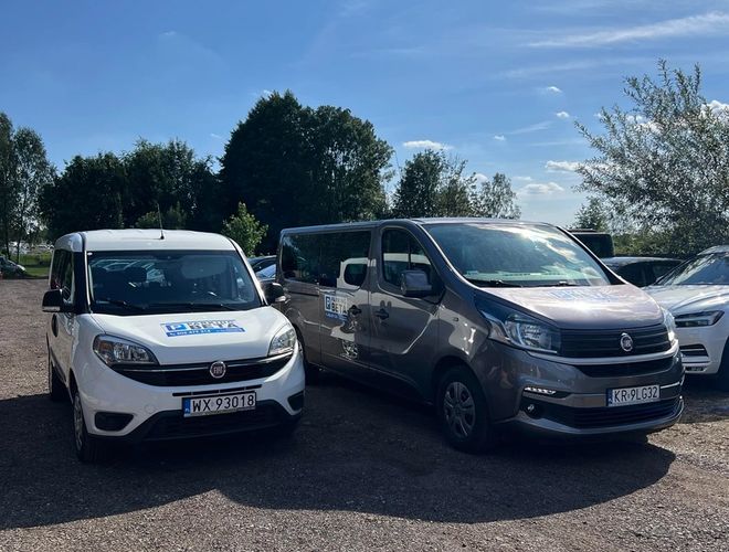 Parking Beta – Na parkingu stoją dwa samochody dostawcze. Jeden jest biały, drugi szary. W tle widoczne są drzewa i niebo.