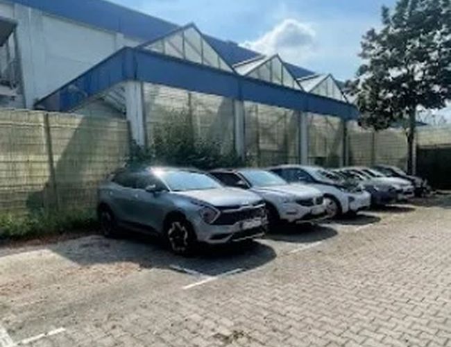 Samochody zaparkowane na brukowanym placu obok budynku z niebieskimi konstrukcjami dachowymi.