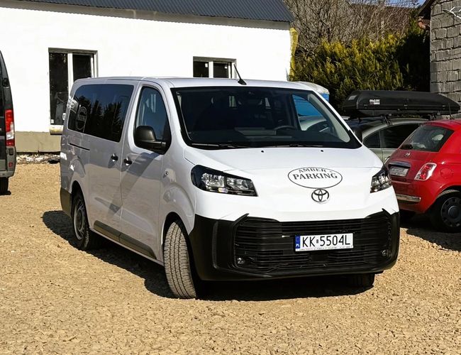 Parking Amber — Na parkingu stoi biały samochód dostawczy. W tle widoczne są inne pojazdy i budynek.