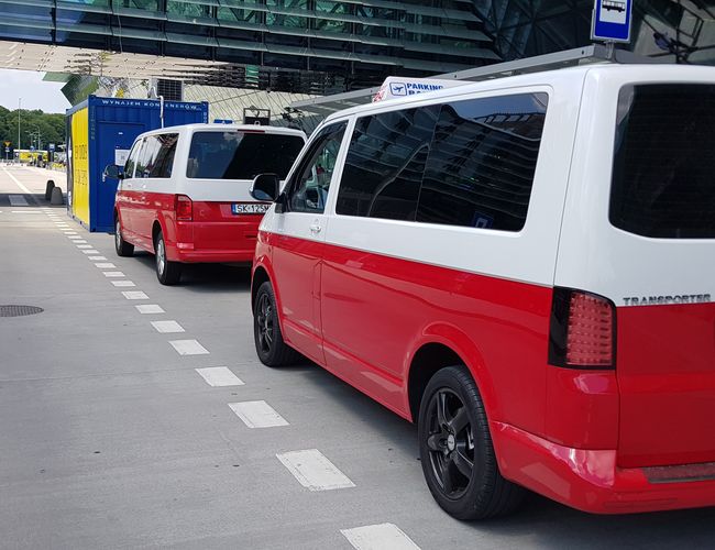 GOOD Parking - Dwa czerwono-białe vany stoją obok chodnika. Nad nimi zadaszenie z przeszklonym dachem.