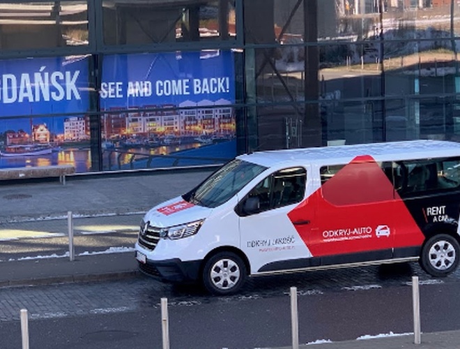 Odkryj-Parking GDN – Bus z logo firmy stoi obok budynku. W tle widoczny jest duży baner z napisem Gdańsk.