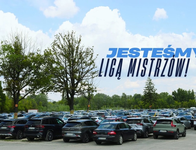 Najlepšia parkovacia séria A – Parkovisko plné zaparkovaných vozidiel. Na pozadí stromy a obloha s oblakmi. Transparent s nápisom "Sme liga majstrov!".