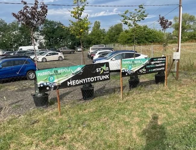 Baner parkingu Star Park Airport Car Park przy wjeździe, z zaparkowanymi samochodami i terenem parkingu w tle.