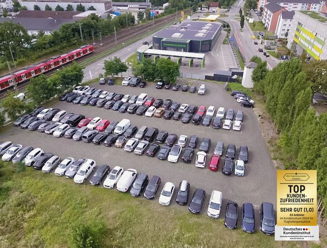 Parkoló Mein-Flughafenparkplatz-Frankfurt P1 – A téren sok autó parkol. A parkolót fákkal és épületekkel vették körül.