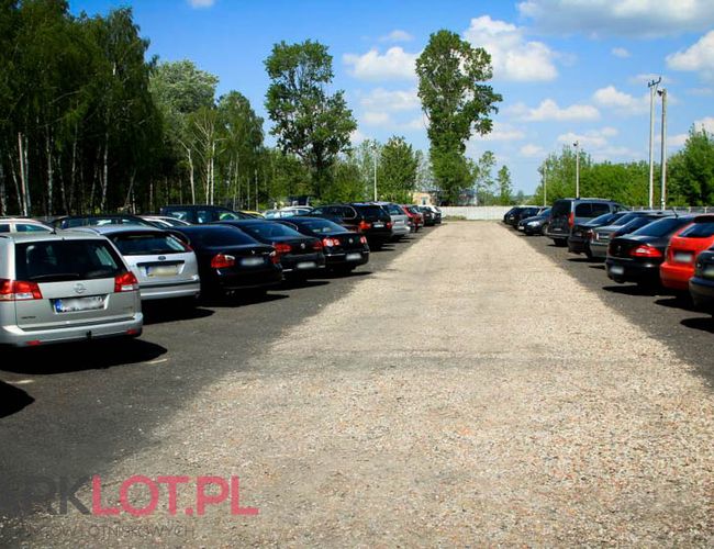 Aparcamiento P38 - en el área pavimentada hay coches. A los lados crecen árboles. Cielo despejado con nubes.