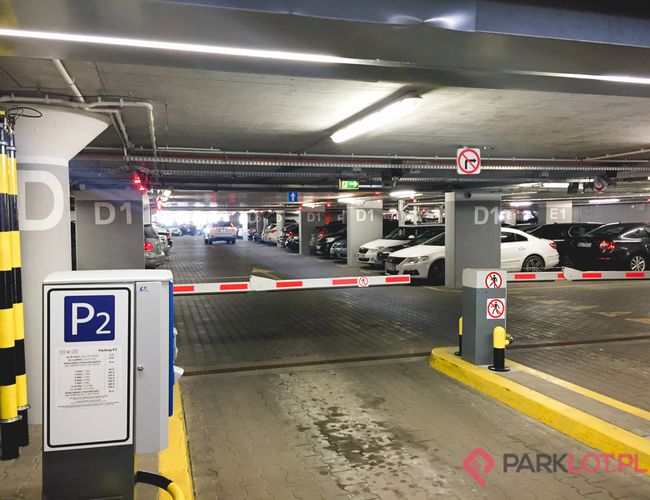 Oficjalny Parking Lotniska P2 – Parking wielopoziomowy, zadaszony i oznakowany. Barierki blokują wjazd. Samochody stoją w rzędach.