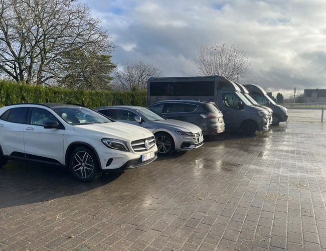 Parking ParkNow Frankfurt – Kilka samochodów stojących na utwardzonym placu. W tle widoczne są drzewa i ogrodzenie. Pogoda pochmurna, ale jasna.