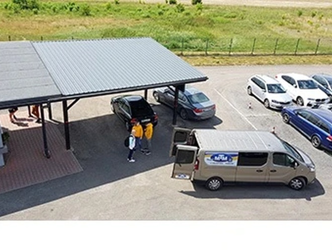 Estacionamiento MTM - Los coches están en un espacio amplio. El área está parcialmente techada y bien acondicionada. La gente conversa junto al coche.