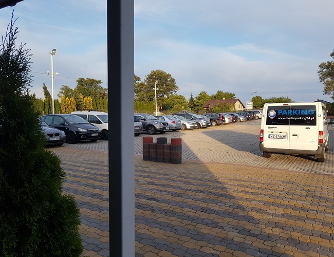 PARKING P24 PREMIUM - Duży, ogrodzony teren. Samochody stoją w rzędach. Lampa oświetla obszar.