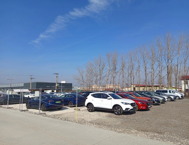 Coches estacionados y una cerca que separa los senderos. En el fondo se ven árboles.
