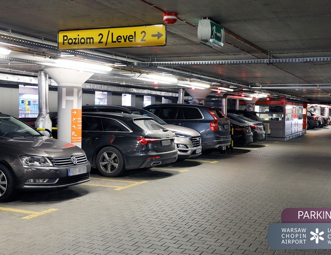 Oficiálne parkovisko Letiska P2 – vnútorné viacposchodové parkovisko. Niekoľko áut zaparkovaných vedľa seba. Na strope sú smerové značky.