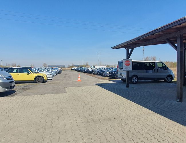 WIZ-PARK - Gran aparcamiento sin cercar de adoquines. Los coches están en filas. A la entrada hay un cobertizo techado.