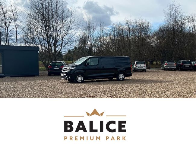 Balice Premium Park – Na żwirowym parkingu stoi kilka samochodów. W tle widać drzewa i ciemny kontener.