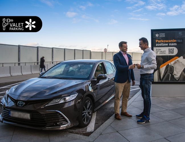 Parkservice – Chopin-Flughafen – Zwei Männer tauschen die Autoschlüssel aus. Nebenan befindet sich ein Infotafel. Blauer Himmel im Hintergrund.
