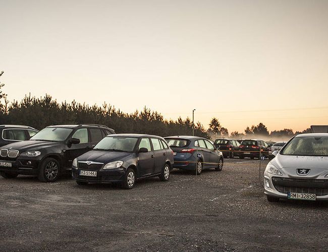 PERI Parking – En el aparcamiento de grava hay muchos coches. Todavía es una mañana temprana. Los árboles al fondo crean un límite natural.