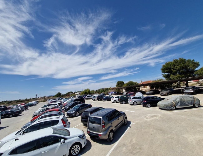 Monster Parking – Na parkovisku stojí veľa vozidiel. Areál je neplánovaný a priestranný. Na oblohe sú vidieť biele oblaky.