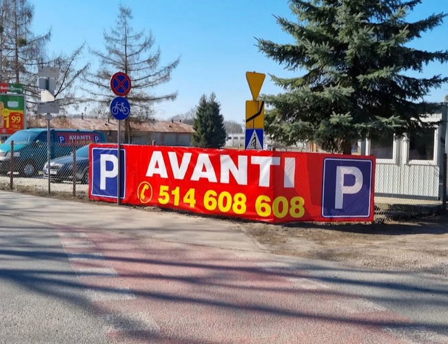 Parkovisko Avanti - Na obrázku je veľký banner s názvom a telefónnym číslom. Vedľa sú dopravné značky a pozemok je oplotený.